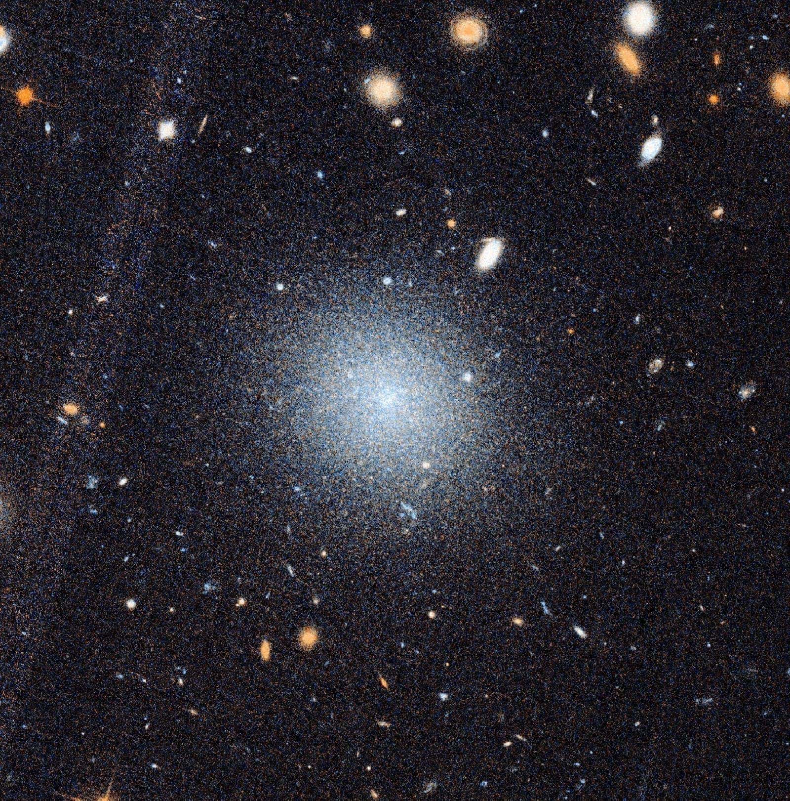 A composite image showing a close-up Hubble Space Telescope view of the ultra-diffuse galaxy NGC 1052-DF9 (inset) below a wider DECaLS survey view of the NGC 1052 region. Blue boxes mark a linear chain of galaxies including DF2, DF4, and the newly discovered DF9. Red outlines show KCWI data collection areas. Credit: Keim et al./DECaLS/HST.