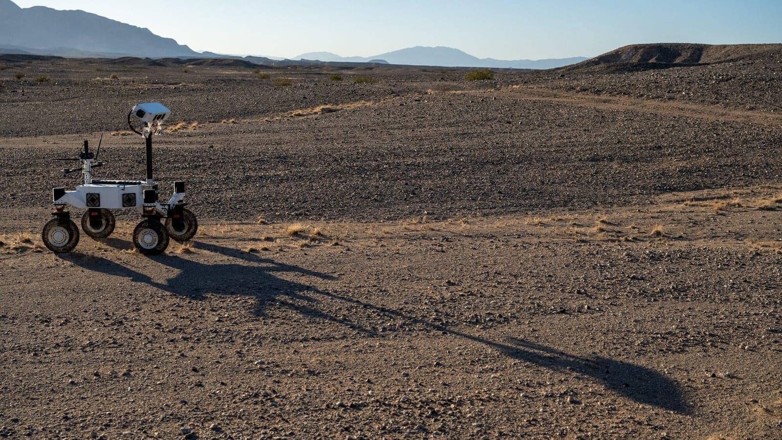 ERNEST rover driving across desert terrain at dawn, casting a long shadow. The test simulated the elongated shadows a rover would encounter in lunar polar regions, where the Sun sits permanently low on the horizon.