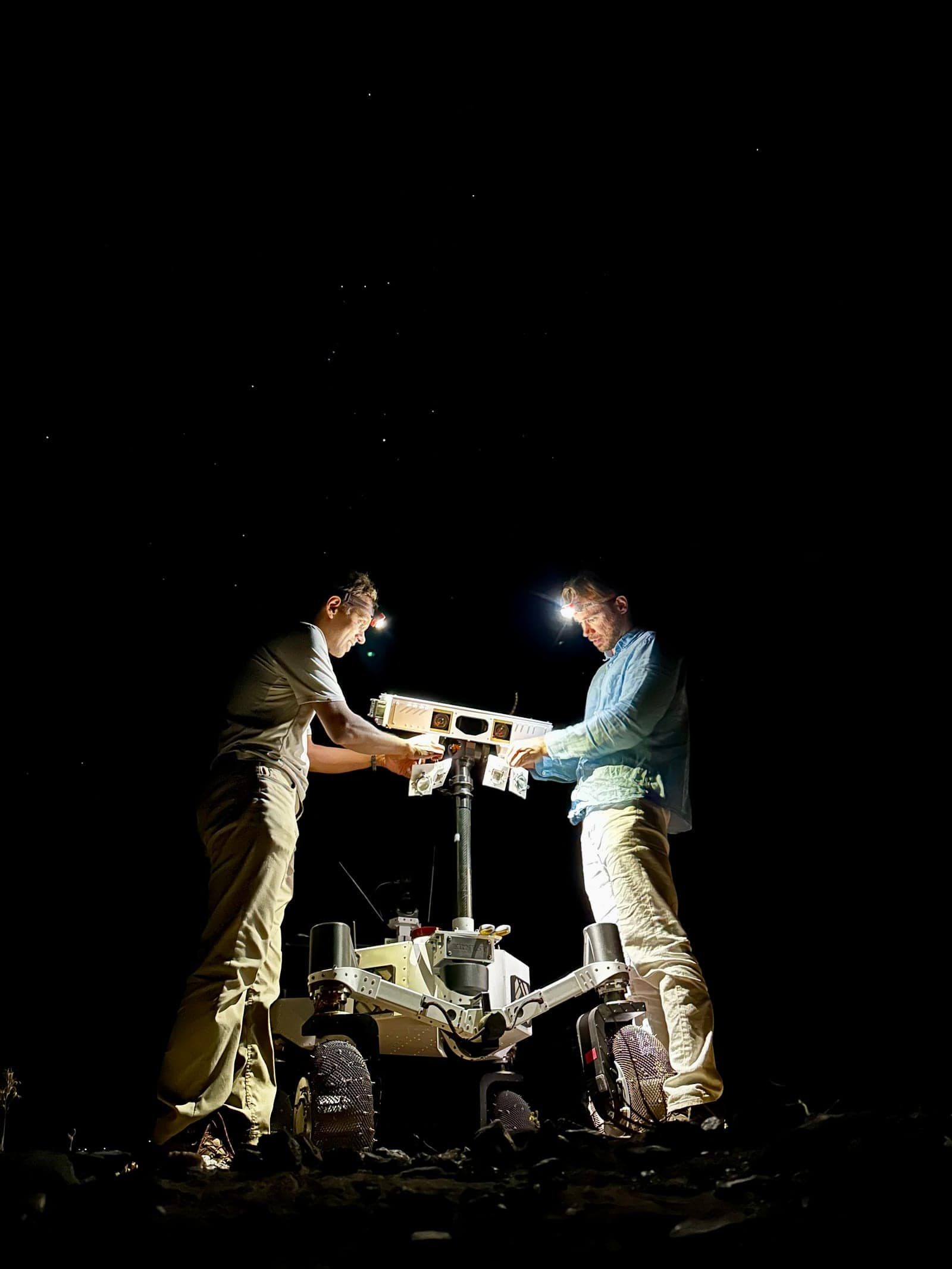 Two JPL engineers setting up illuminators on the ERNEST rover at night in the Colorado Desert. The night testing verified that the rover's autonomous navigation could handle complete darkness, a requirement for operating in permanently shadowed lunar polar craters.