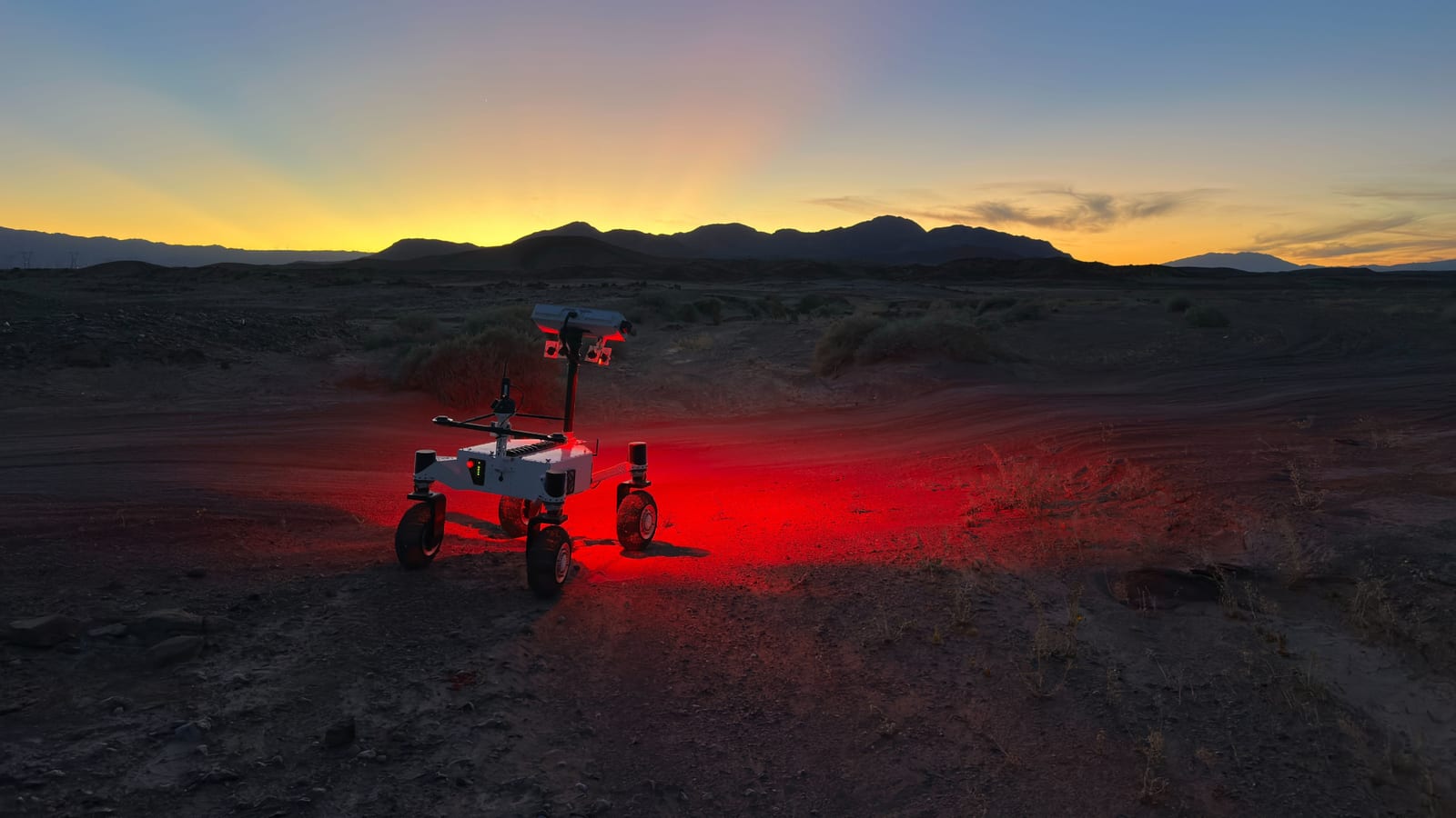 NASA's ERNEST rover prototype driving across the Colorado Desert near Plaster City, California during a March 2026 field test. The compact four-wheeled rover has a rectangular mast and mesh wheels with active suspension that can lift independently over obstacles. Credit: NASA/JPL-Caltech.