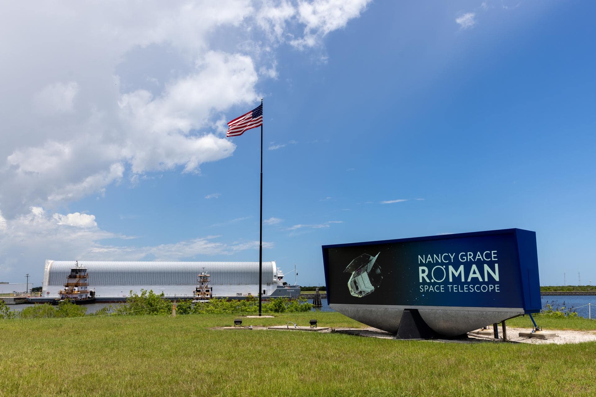 Another view of the Pegasus barge docking at Kennedy Space Center, showing the shipping container housing the Roman telescope with workers and equipment on the dock
