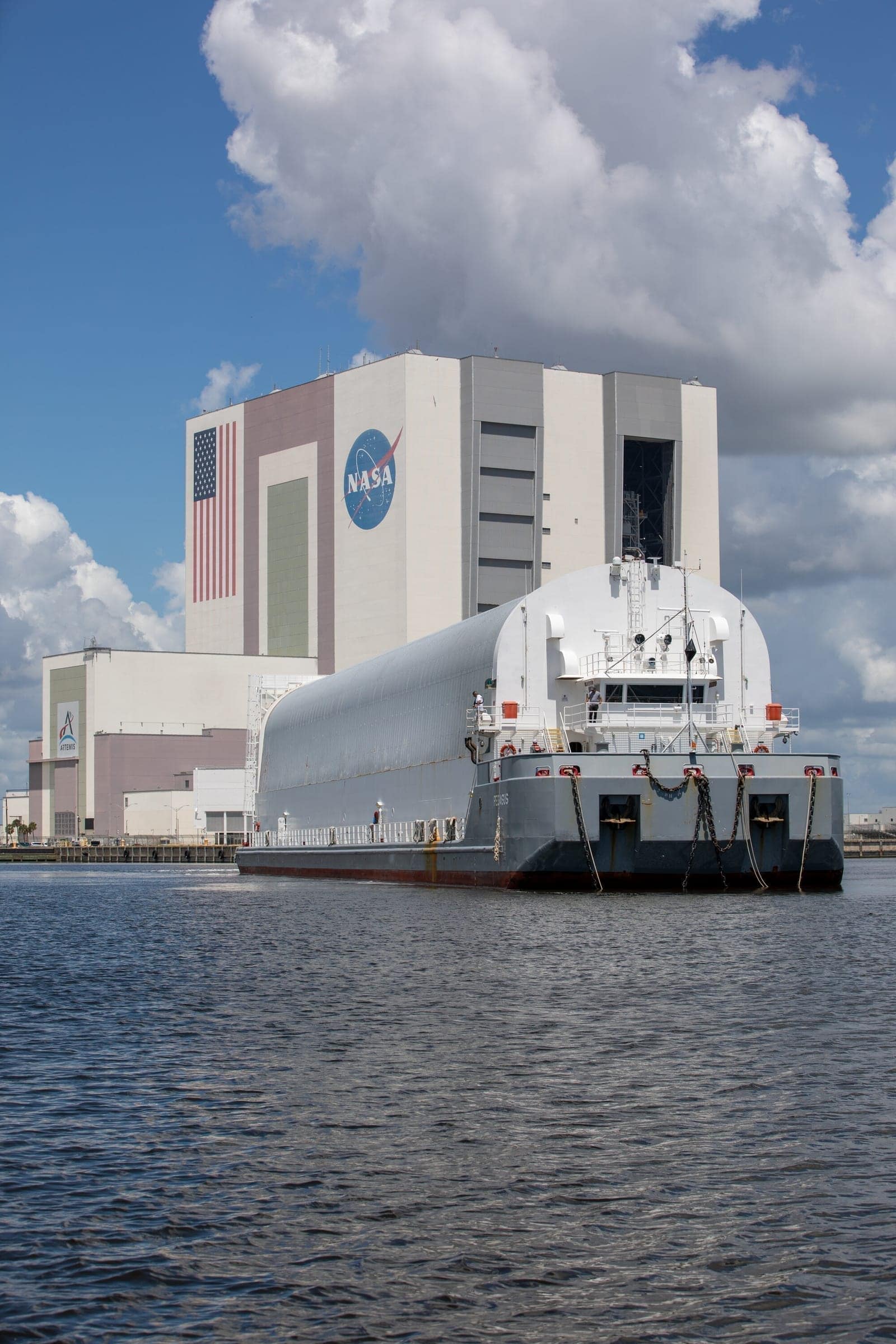 NASA's Pegasus barge carries the Nancy Grace Roman Space Telescope in its shipping container into the Launch Complex 39 turn basin at Kennedy Space Center in Florida on June 21, 2026. The Vehicle Assembly Building is visible in the background. Credit: NASA/Amber Jean Notvest.