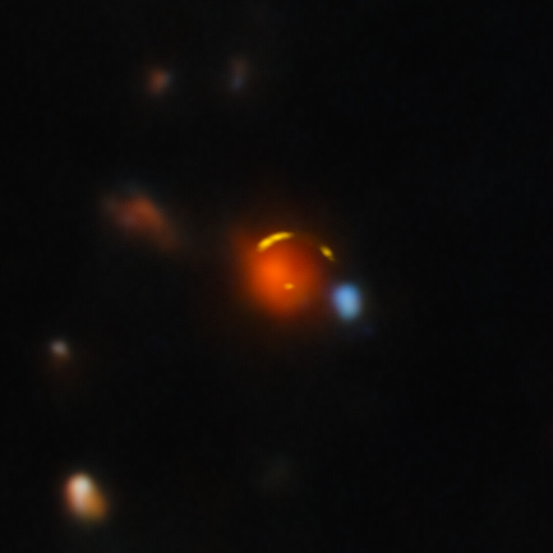 The gravitationally lensed galaxy 'Shadow Blaster' (JCMT0402-0424), showing a red foreground elliptical galaxy with yellow arcs representing four distorted images of the distant starburst galaxy behind it. Gemini North and ALMA composite. Credit: International Gemini Observatory / NOIRLab / NSF / AURA / ALMA (ESO / NAOJ / NRAO).