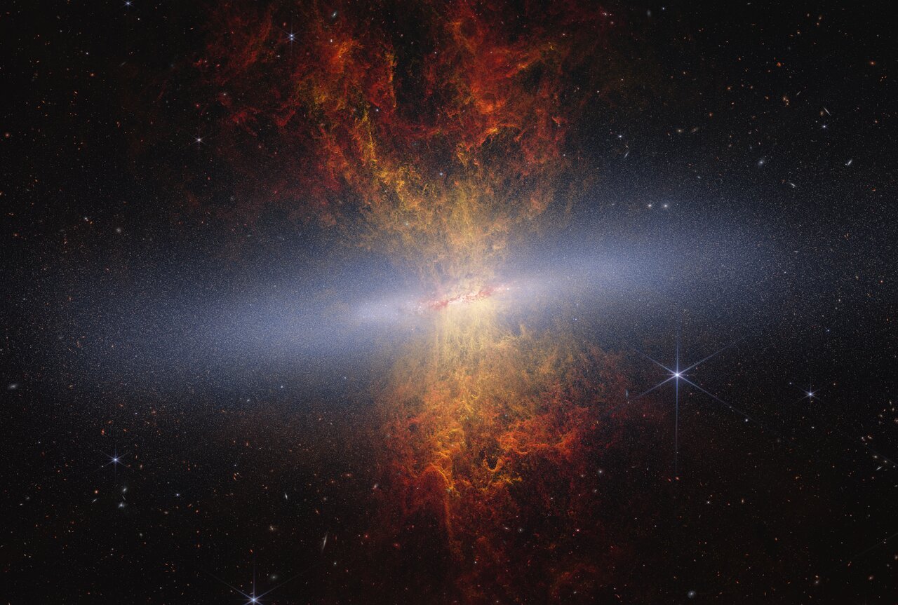 Composite image of edge-on starburst galaxy M82 from Webb and Hubble. The galaxy appears as a bright horizontal streak against black space, filled with blue-white stars resolved by Webb. Yellow and orange outflow plumes extend above and below the disk. Credit: NASA, ESA, CSA, A. Smercina (STScI), T. Williams (University of Manchester). Image processing: A. Pagan (STScI).