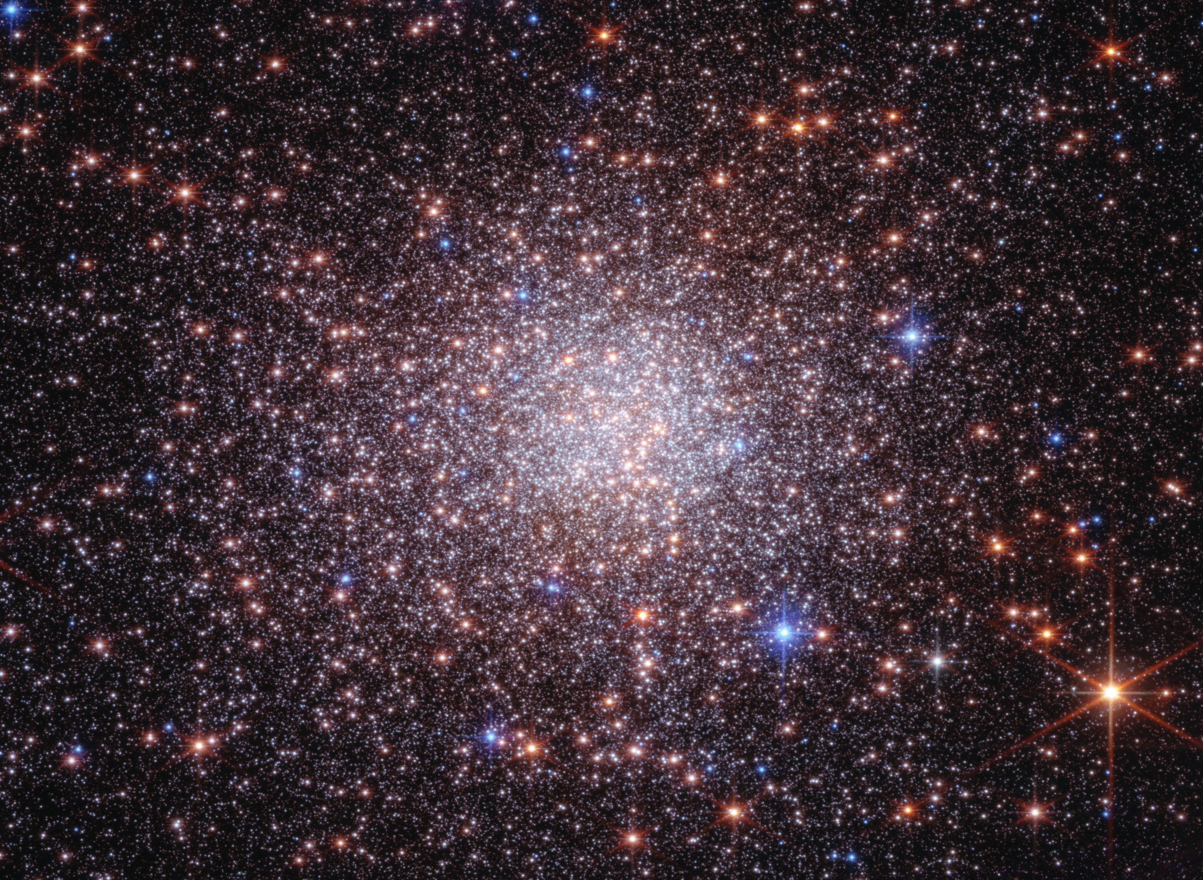 A composite near-infrared and optical image of the stellar system Terzan 5, showing thousands of stars packed densely together against the dusty backdrop of the Milky Way central bulge